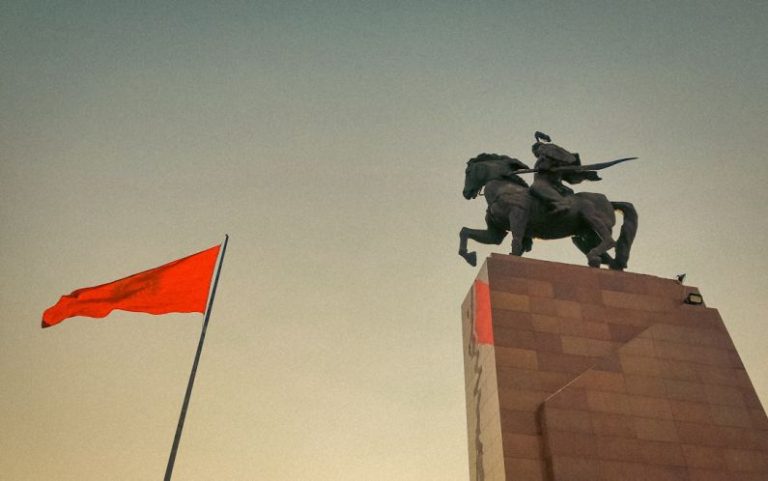 Hero Horse - a statue of a man riding a horse next to a red flag